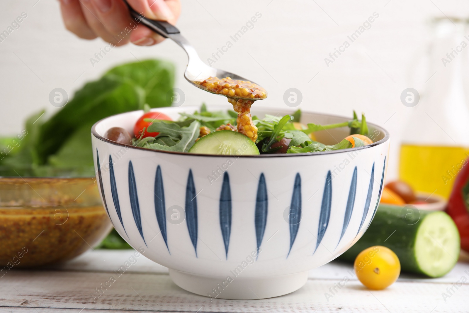 Photo of Woman pouring tasty vinegar based sauce (Vinaigrette) from spoon into bowl with salad at wooden rustic table, closeup