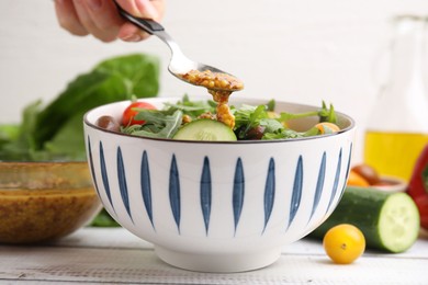 Photo of Woman pouring tasty vinegar based sauce (Vinaigrette) from spoon into bowl with salad at wooden rustic table, closeup