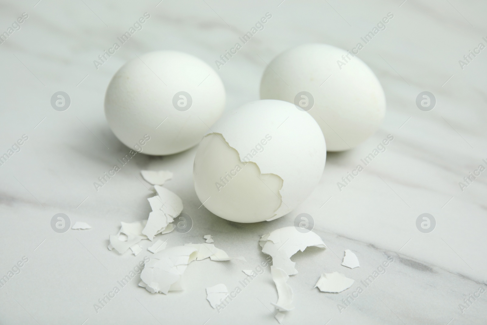Photo of Boiled chicken eggs and pieces of shell on white marble table