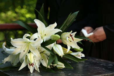 Photo of People near white lilies on granite tombstone at cemetery outdoors, closeup. Funeral ceremony