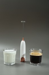 Photo of Mini mixer (milk frother) between glasses of coffee and milk on grey background