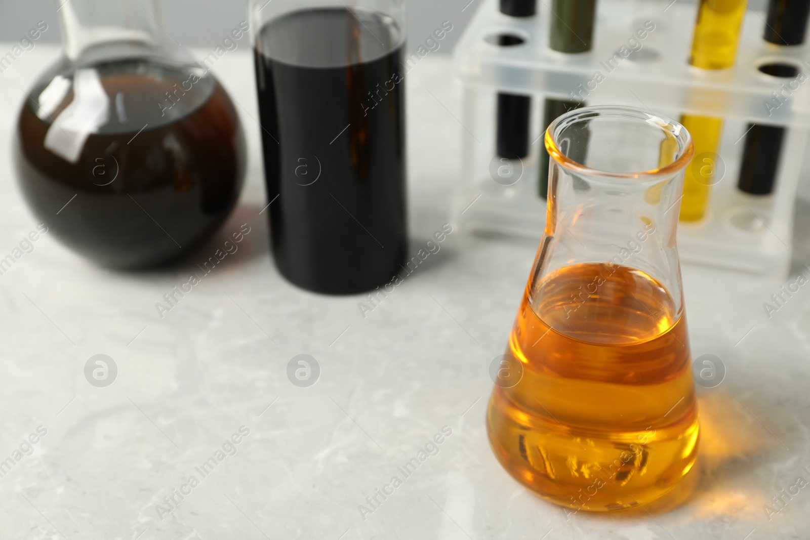 Photo of Laboratory glassware with different types of oil on white table, closeup. Space for text