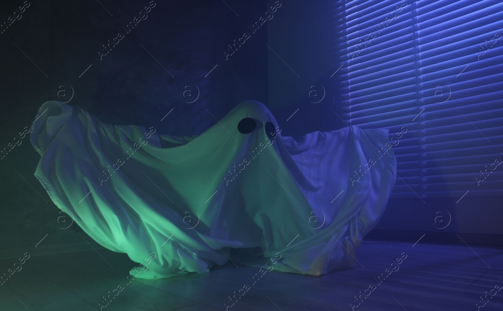 Photo of Creepy ghost. Woman covered with sheet near window in blue light