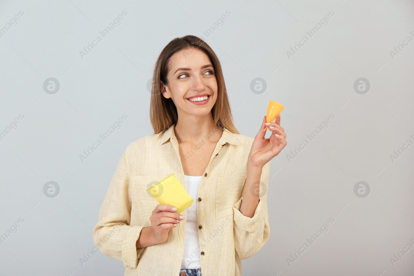 Photo of Happy young woman with menstrual cup and disposable pad on grey background