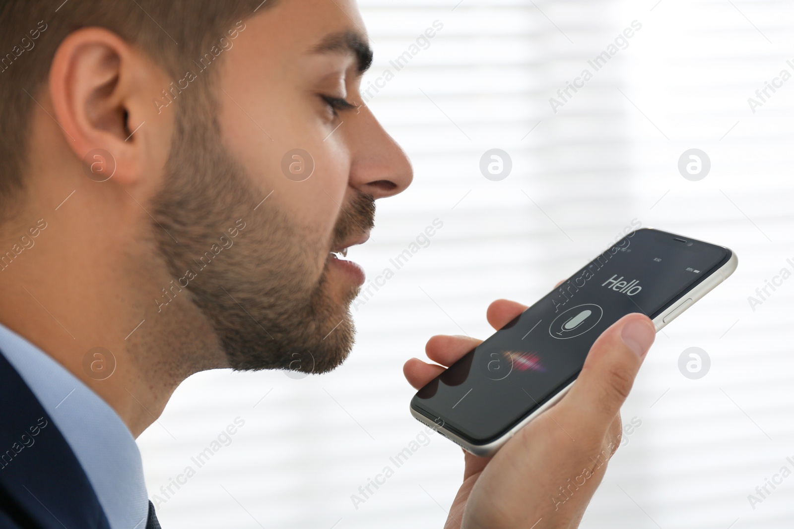 Photo of Young man using voice search on smartphone indoors, closeup