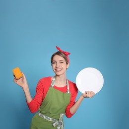 Young housewife with plate and sponge on light blue background