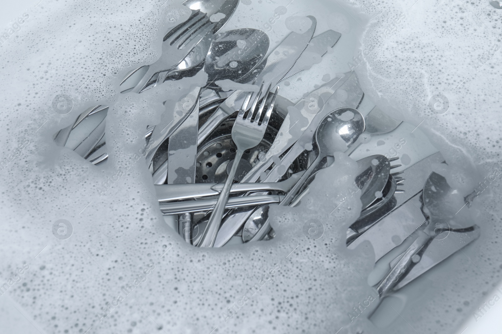 Photo of Washing silver spoons, forks and knives in water with foam, above view