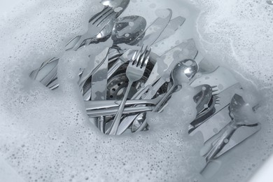 Photo of Washing silver spoons, forks and knives in water with foam, above view