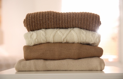 Stack of folded warm sweaters on white table indoors