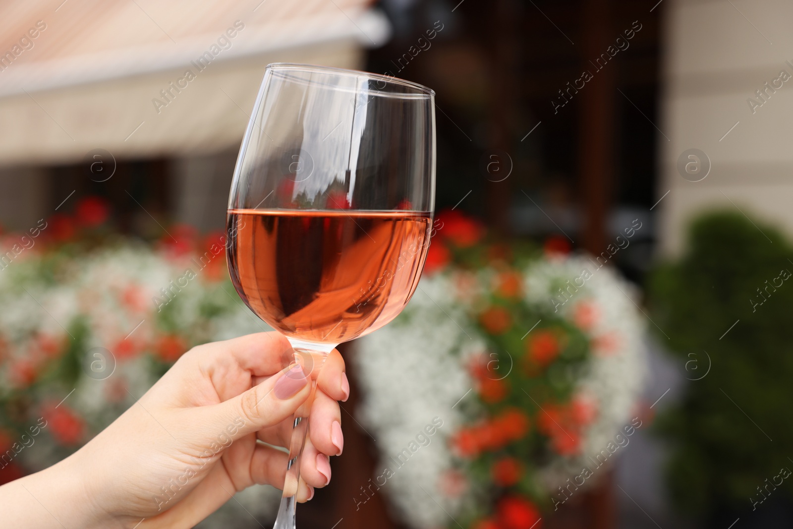 Photo of Woman holding glass of rose wine outdoors, closeup. Space for text