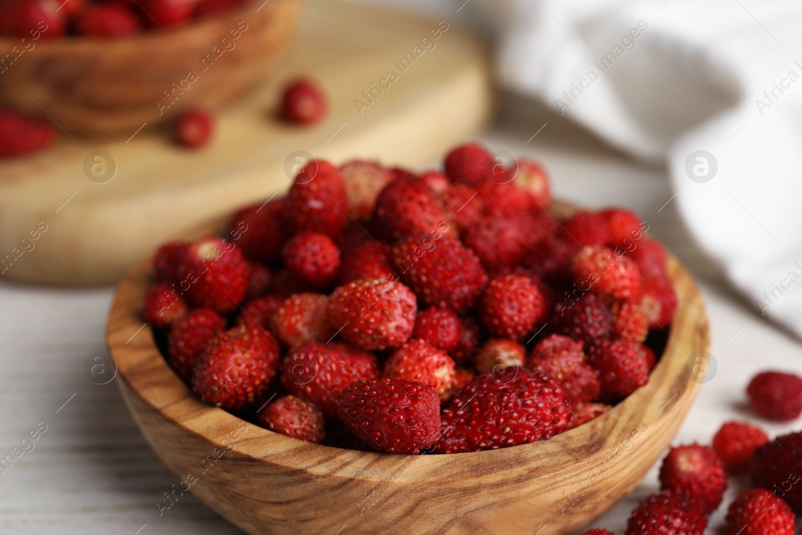 Photo of Fresh wild strawberries in bowl on white wooden table, closeup