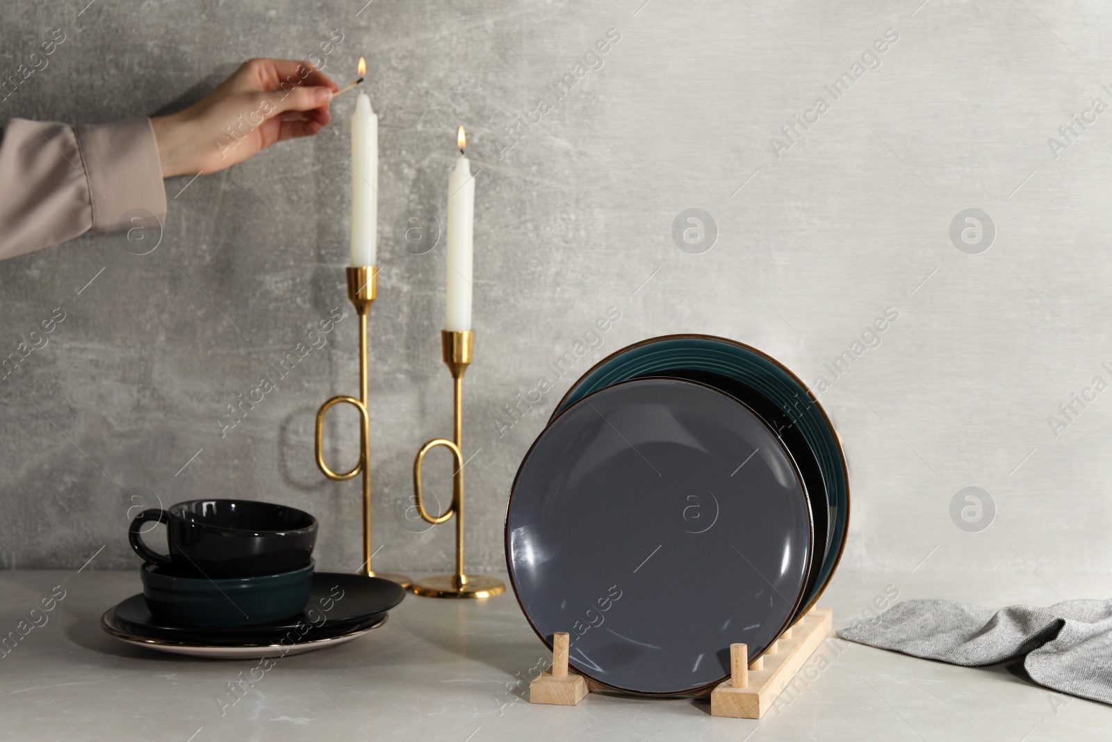 Photo of Woman lighting candle near set of dishware on grey marble table, closeup