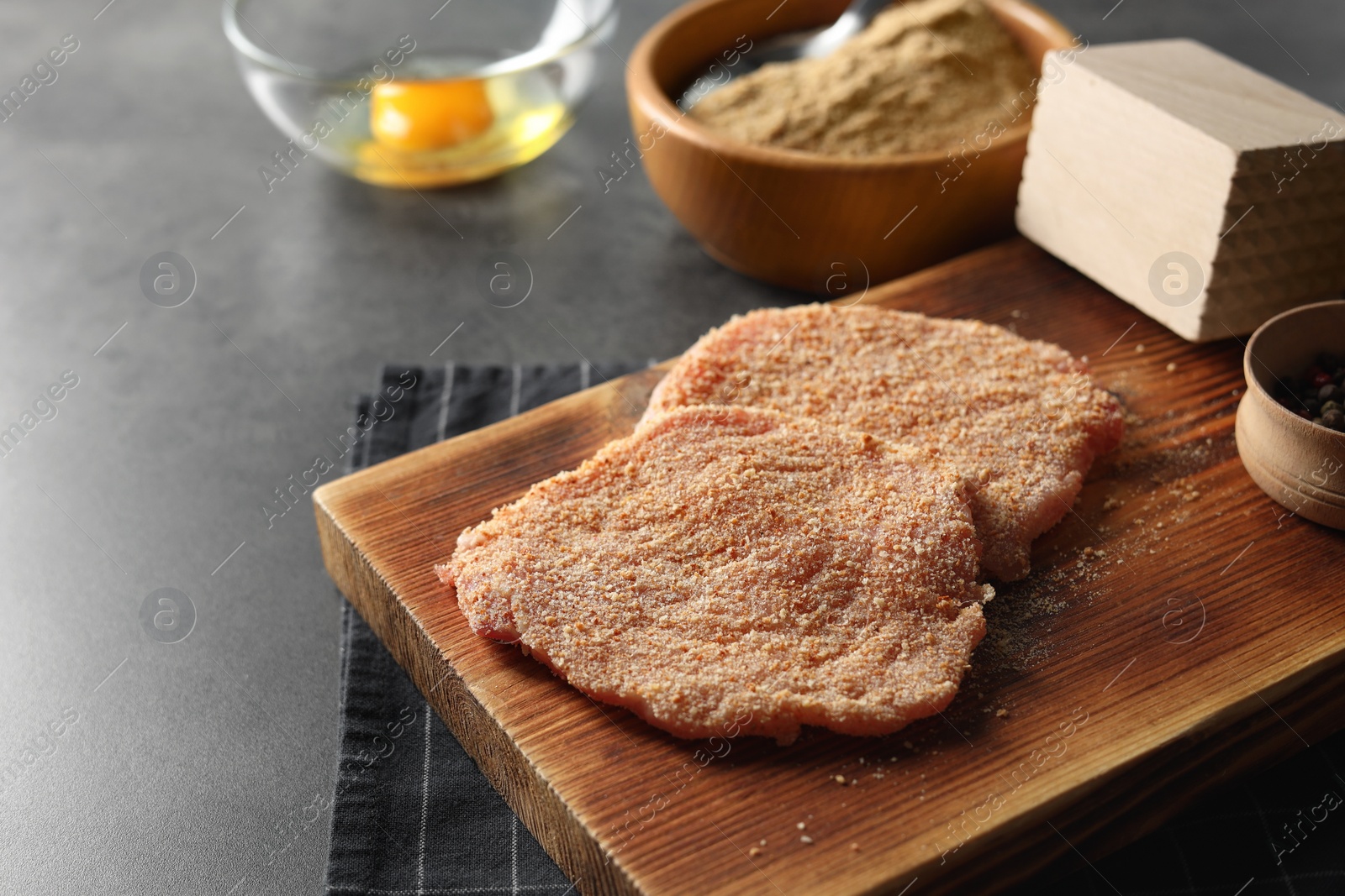 Photo of Cooking schnitzel. Board with raw breaded pork slices on grey table