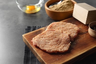 Photo of Cooking schnitzel. Board with raw breaded pork slices on grey table