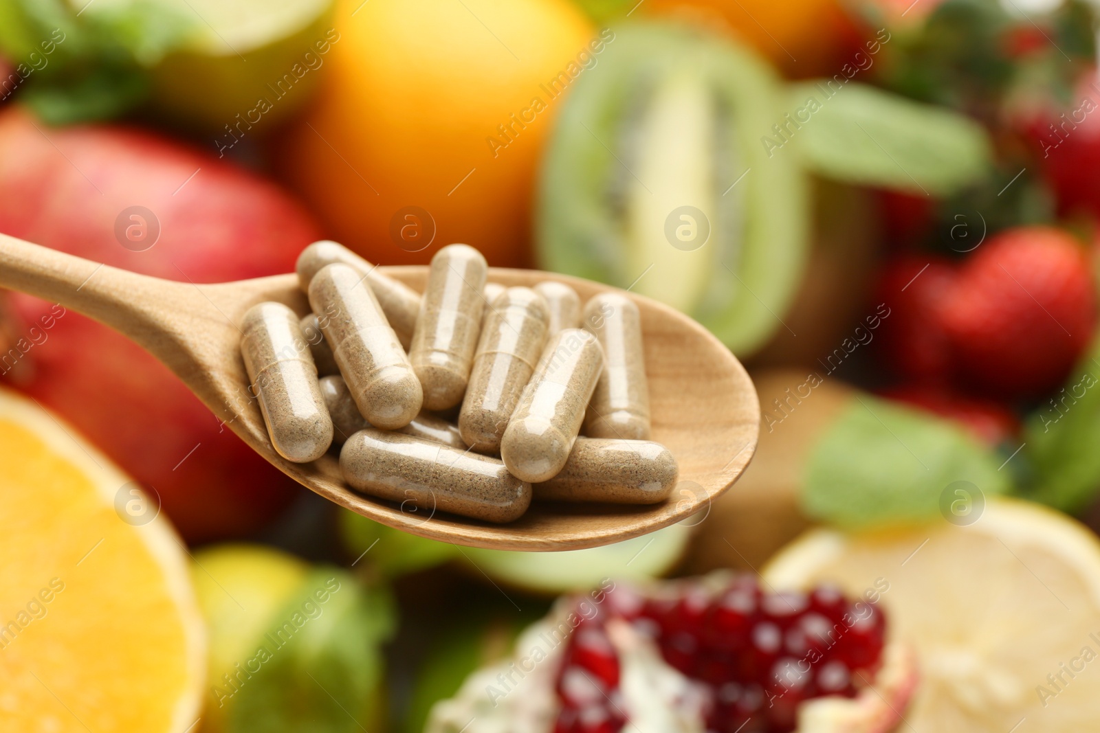 Photo of Vitamin pills in spoon against fresh fruits, closeup