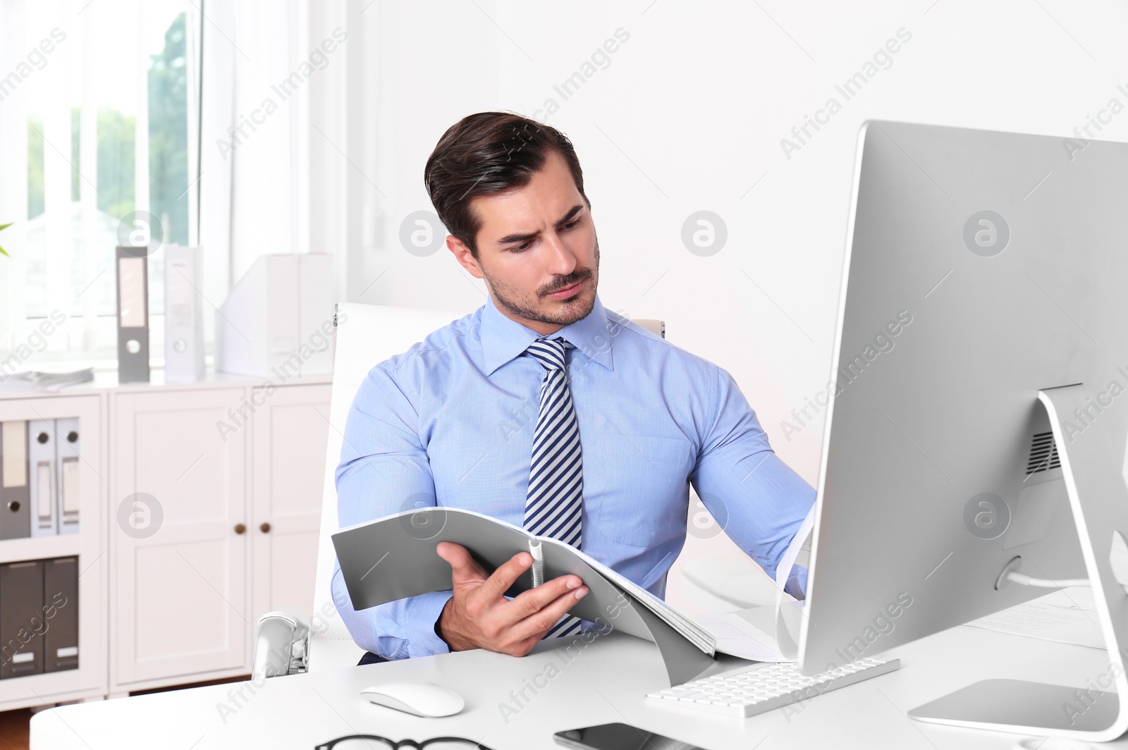 Photo of Handsome young man working with notebook and computer at table in office