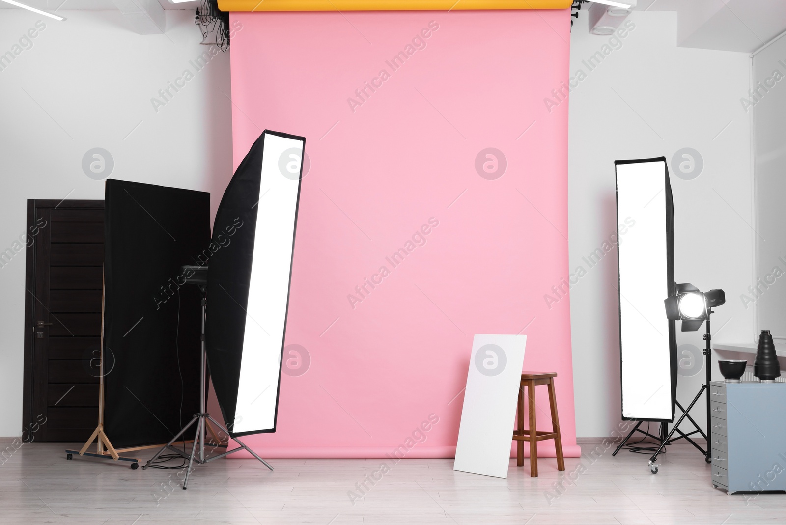 Photo of Pink photo background, stool and professional lighting equipment in studio