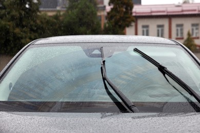 Photo of Car wipers cleaning water drops from windshield glass outdoors, closeup