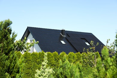 Photo of Modern house with black roof and green trees outdoors on sunny day