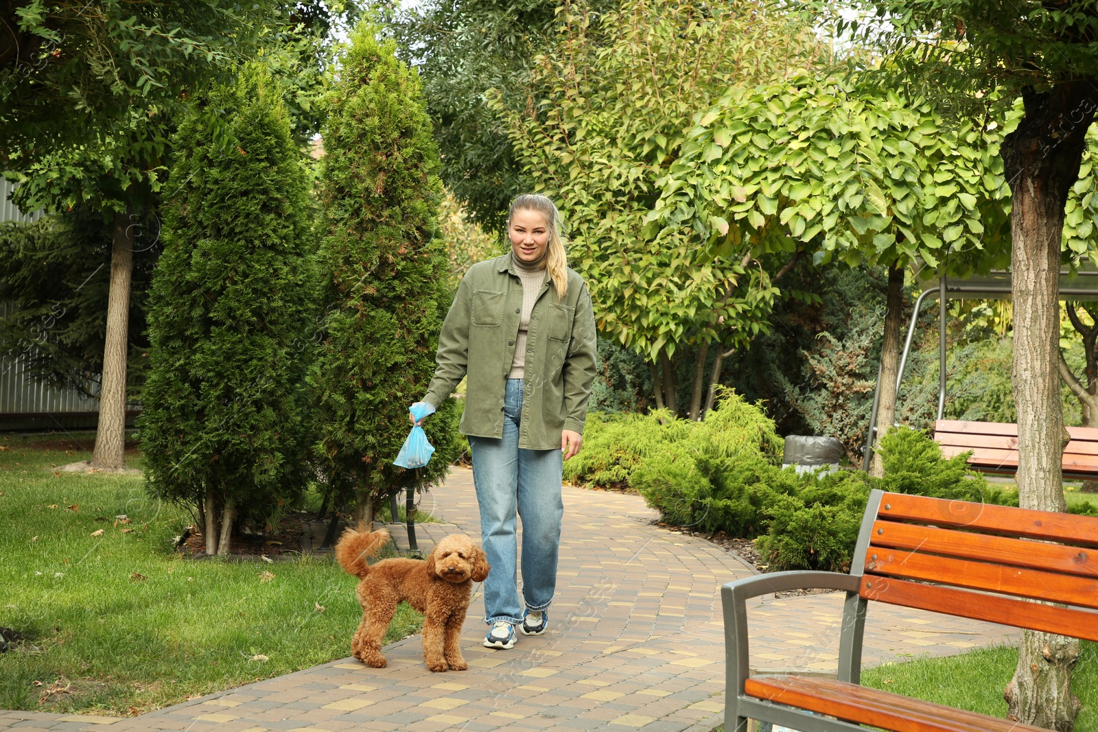 Photo of Woman with waste bag walking her Maltipoo cute dog in park