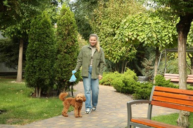 Photo of Woman with waste bag walking her Maltipoo cute dog in park