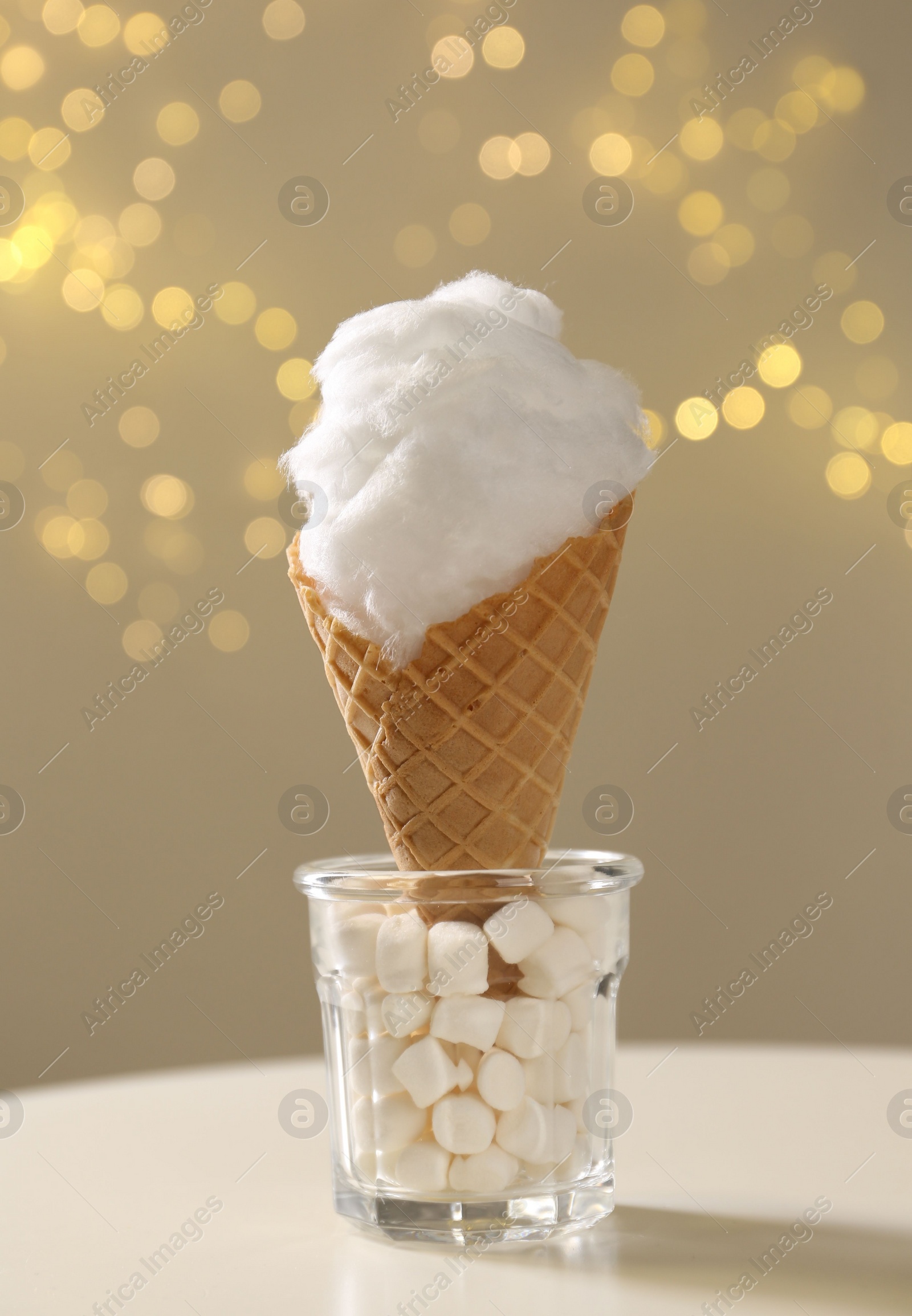 Photo of Sweet cotton candy in waffle cone on table against blurred lights