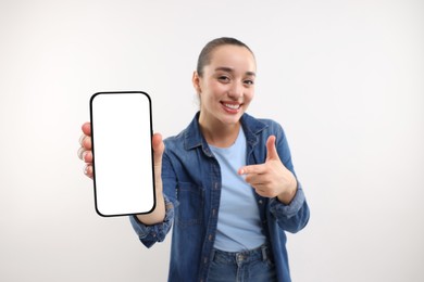 Young woman showing smartphone in hand and pointing at it on white background, selective focus. Mockup for design