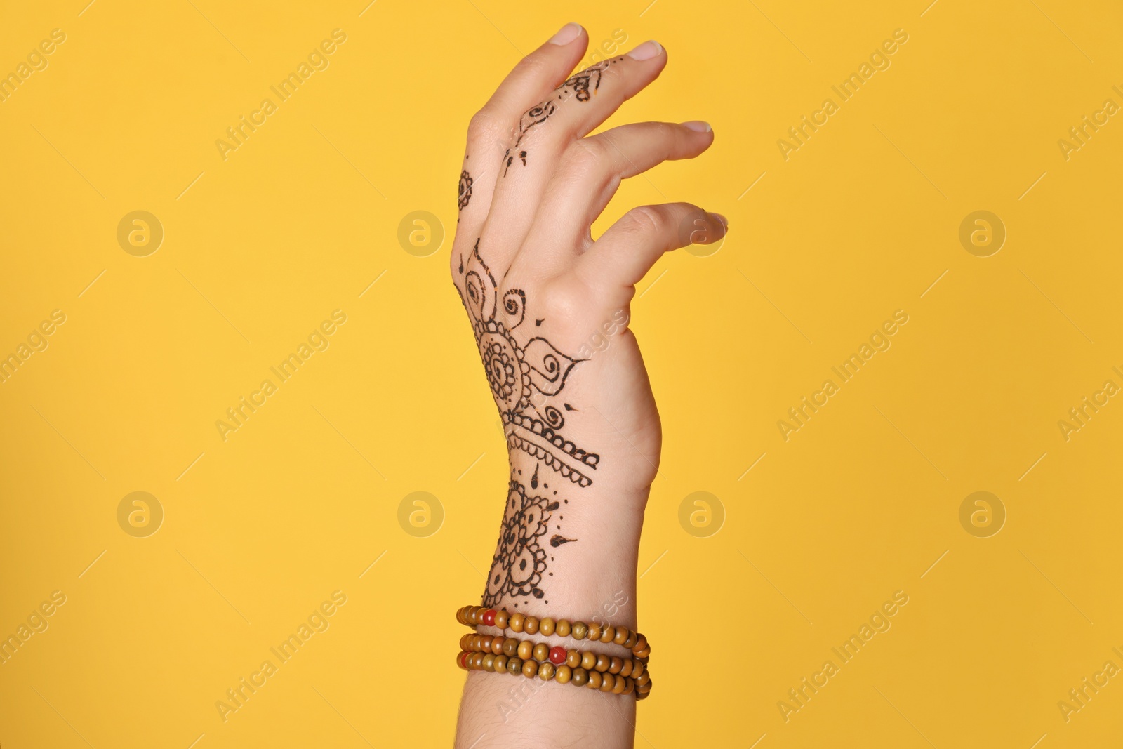 Photo of Woman with beautiful henna tattoo on hand against yellow background, closeup. Traditional mehndi