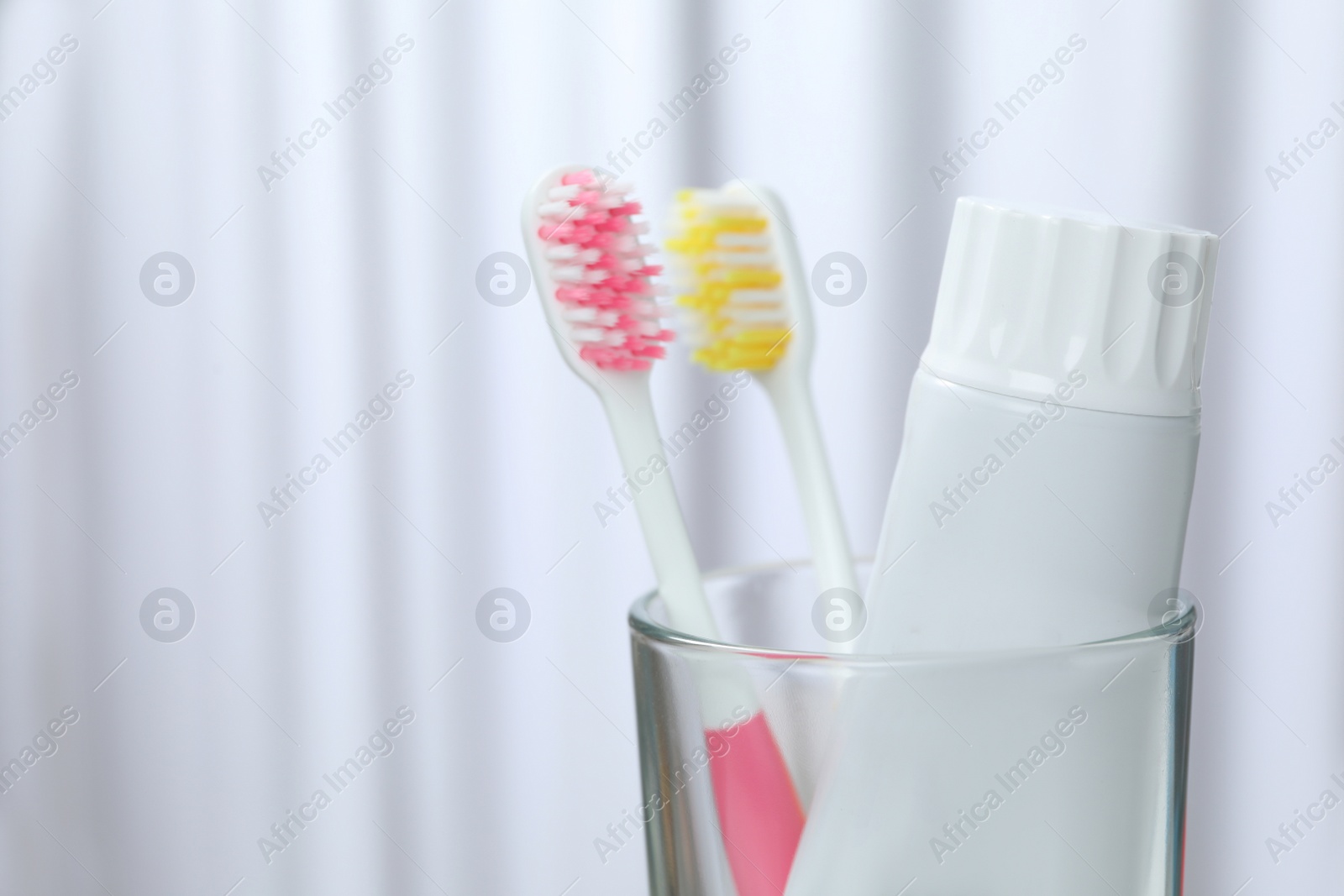 Photo of Glass with brushes and toothpaste on blurred background. Space for text