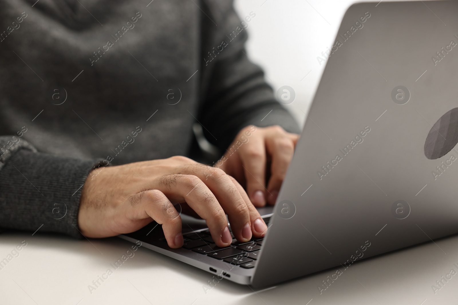 Photo of E-learning. Young man using laptop at white table, closeup