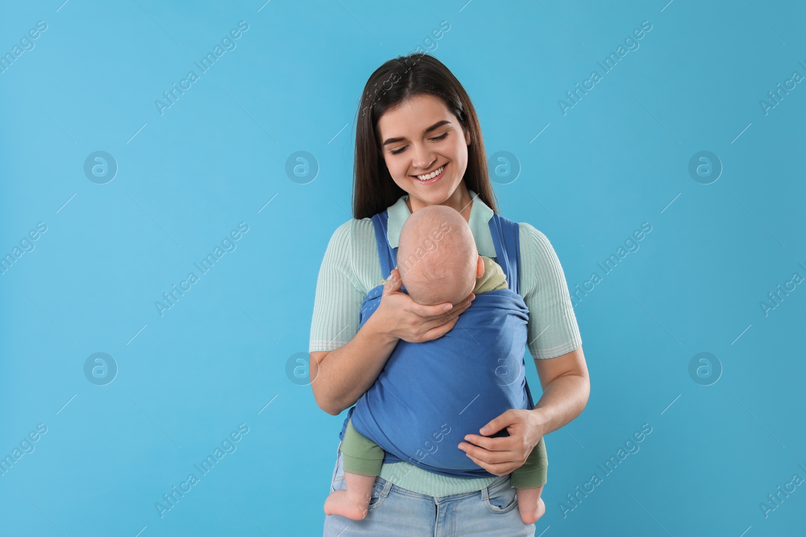 Photo of Mother holding her child in sling (baby carrier) on light blue background