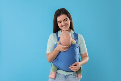 Photo of Mother holding her child in sling (baby carrier) on light blue background