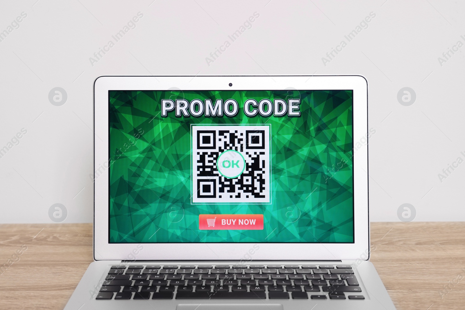 Photo of Laptop with activated promo code on wooden table near white wall