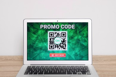 Photo of Laptop with activated promo code on wooden table near white wall