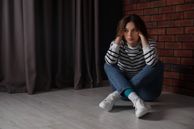 Photo of Sad young woman sitting on floor indoors, space for text