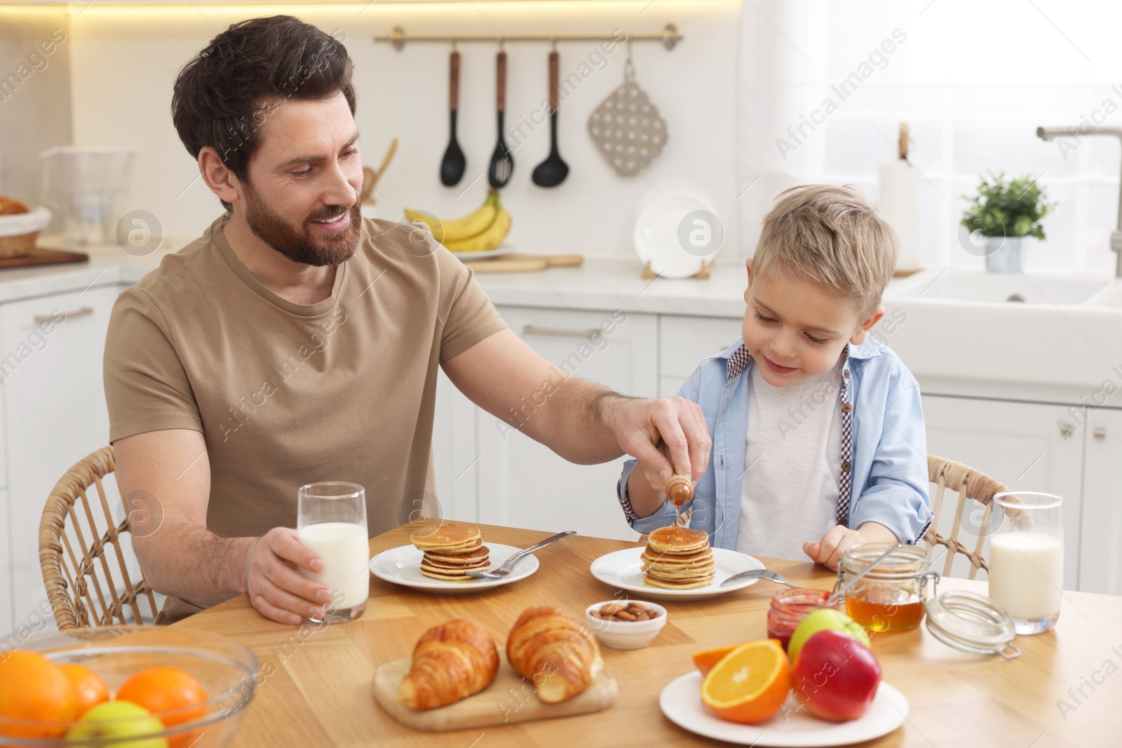 Photo of Father and his cute little son having breakfast at table in kitchen