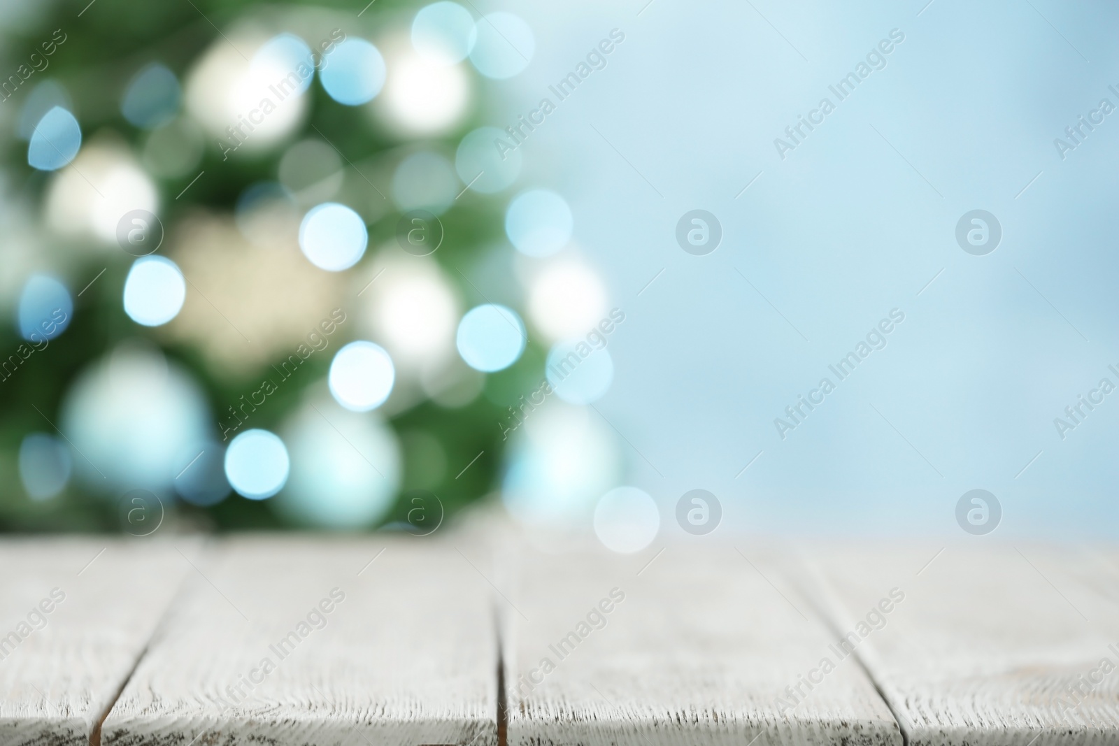 Photo of Empty white wooden table and blurred fir tree with Christmas lights on background, bokeh effect. Space for design