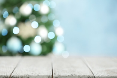 Photo of Empty white wooden table and blurred fir tree with Christmas lights on background, bokeh effect. Space for design