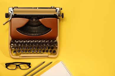 Vintage typewriter, glasses and stationery on yellow background, flat lay. Space for text