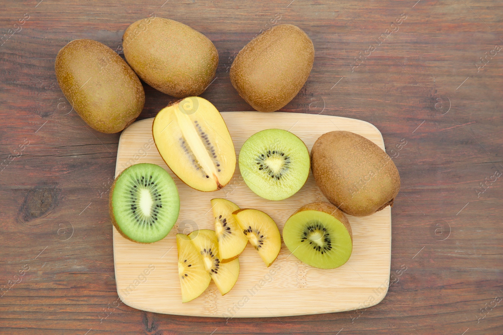 Photo of Whole and cut fresh kiwis on wooden table, flat lay