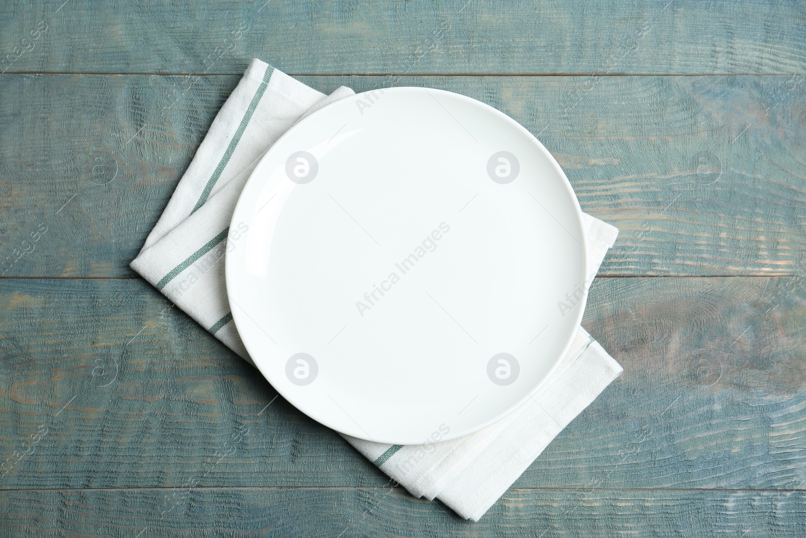 Photo of Empty plate and napkin on blue wooden table, flat lay