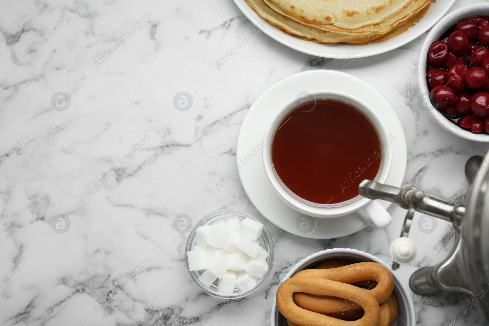 Photo of Metal samovar with cup of tea and treats on white marble table, flat lay. Space for text