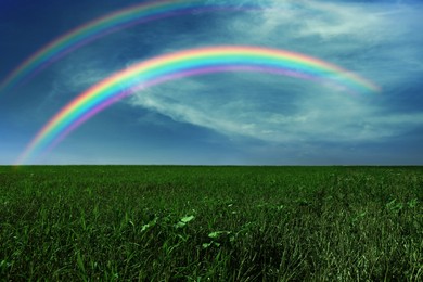 Image of Picturesque view of green meadow and beautiful rainbows in blue sky on sunny day