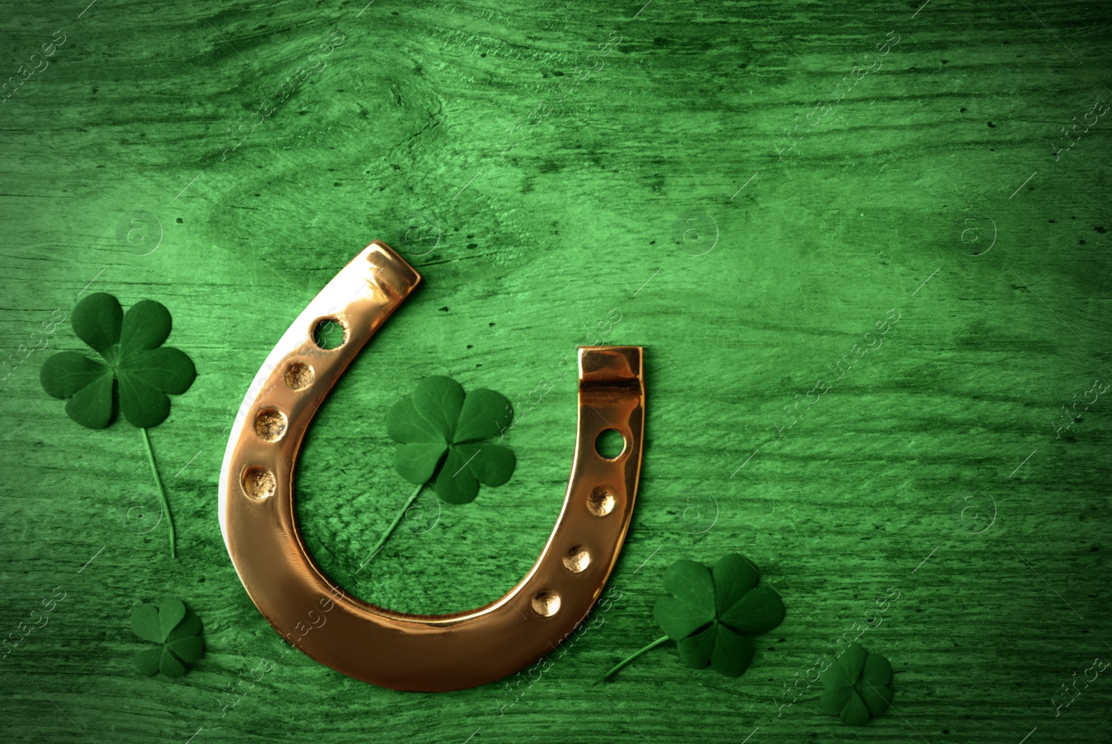 Image of Clover leaves and horseshoe on green wooden table, flat lay. St. Patrick's Day celebration