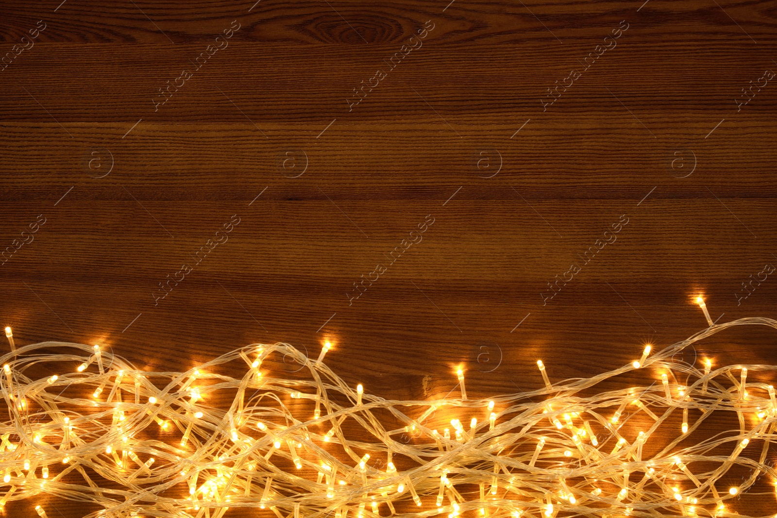 Photo of Beautiful glowing Christmas lights on wooden table, top view. Space for text