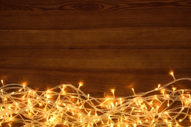 Photo of Beautiful glowing Christmas lights on wooden table, top view. Space for text