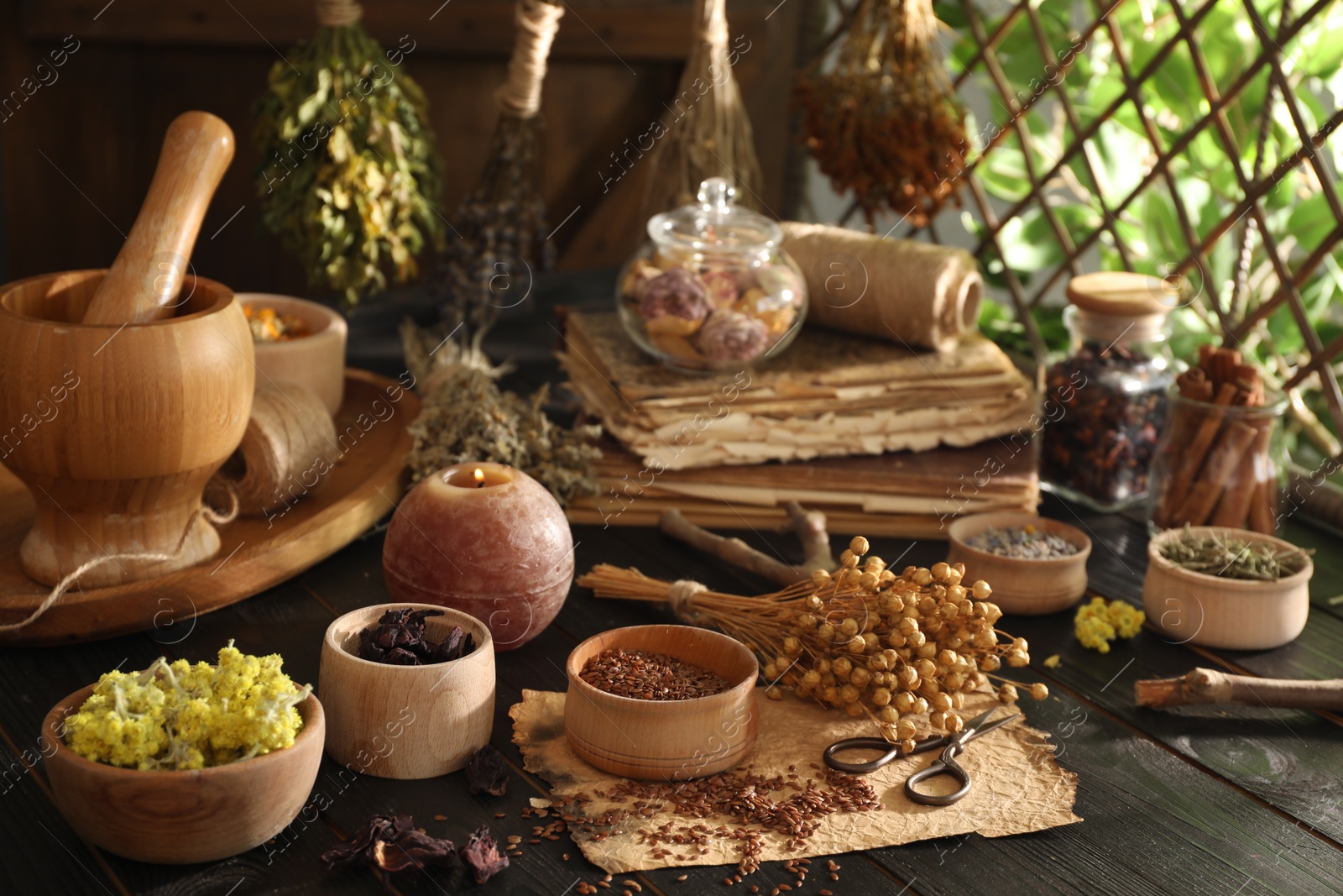 Photo of Different dry herbs, flowers, burning candle and scissors on black wooden table indoors