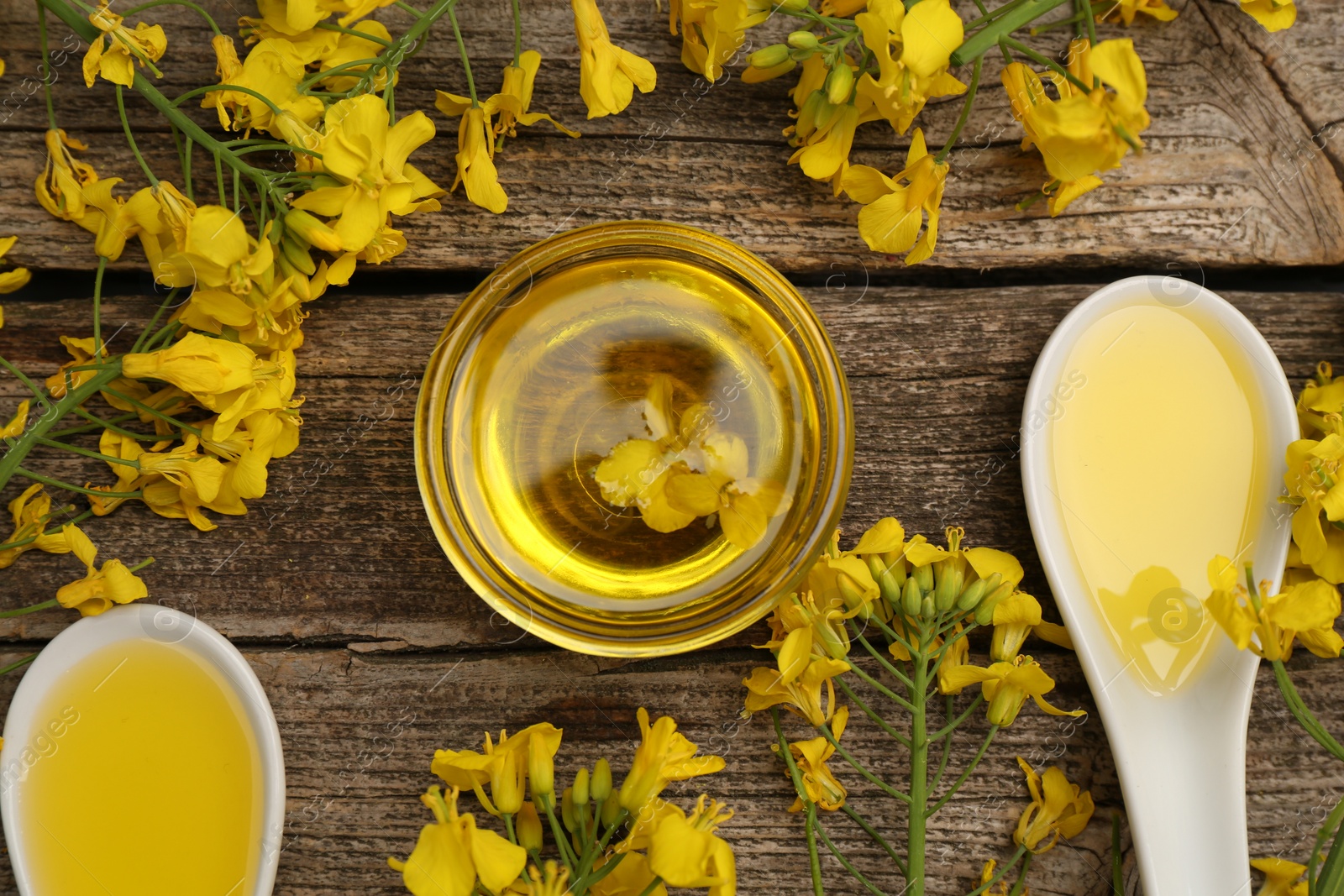 Photo of Rapeseed oil in bowl, gravy boats and beautiful yellow flowers on wooden table, flat lay