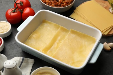 Photo of Cooking lasagna. Pasta sheets in baking tray and products on dark table, closeup