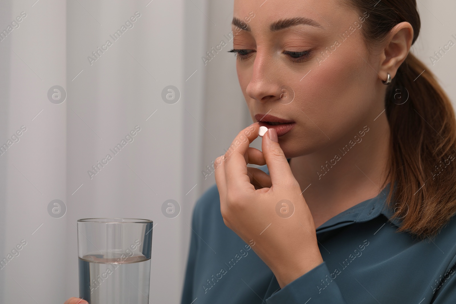 Photo of Woman with glass of water taking antidepressant pill on light background, closeup. Space for text